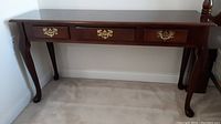Front view of the wood and press board side table with 3 drawers and brass handles.