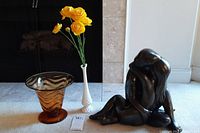 Lot showing amber glass vase, milk glass vase with yellow faux flowers, and bronze statue seated with face covered.