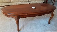 Full view of wooden coffee table showing overall shape, curved edges, and four cabriole legs on carpeted floor.