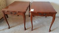 Two medium brown wood end tables with 4 cabriole legs and scalloped edges, positioned side by side on carpet.