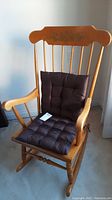 Full view of wooden rocking chair with cushions and floral painted backrest.