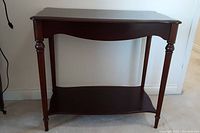 Front view of the wooden side table showing the curved top, turned legs, and lower shelf.