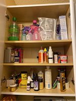 Cupboard with three shelves, showing spray bottles, detergent, paste wax, and cleaner containers.