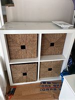 Full front view of white cube shelf with four woven storage bins inserted in compartments, showing overall condition and storage bins.