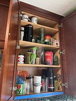 Kitchen cabinet shelves with various mugs, cups, wine glasses, and thermos bottles arranged inside.