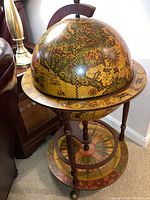 Full view of the antique style globe liquor cabinet next to furniture, showing the detailed ancient map and zodiac ring on the globe and stand.