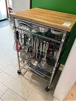 Side view of metal rolling cart with wooden top and hanging kitchen utensils on hooks