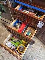 Photo showing opened wooden drawers with various kitchen utensils including graters, juicers, peelers, and bag clips.