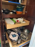 Kitchen cabinet with drawers holding various kitchenware including mixing bowls, cake pans, utensils, and electric appliances.