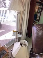 Photo showing the brass floor lamp standing near a window with fabric shade, shade still wrapped in plastic.