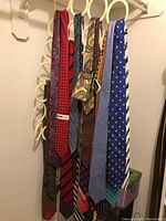 Photo showing a variety of men's neckties hanging, displaying different colors and patterns including paisley, checks, stripes, and geometric prints.