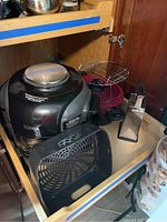 Black Ninja Foodi multi-cooker with pasta pot insert, metal rack, and grater on a pull-out shelf in cabinet.