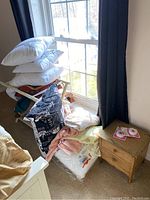 Stack of multiple king size pillows, assorted linens folded and stacked beside a small wooden chest.