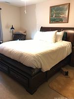 Full view of queen size dark wood sleigh bed made with white bedding, showing headboard, footboard, and storage drawers on the side.