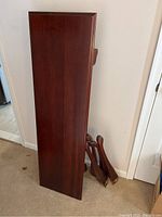 Rectangular wooden table top with smooth cherry finish, viewed from above showing the surface and detached legs leaning beside it.