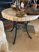 Full view of round stone-tiled table top with decorative bowl and figurines on it, showing the right black iron curved base.