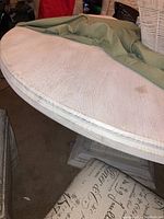 Photo of round tabletop with visible faux wood grain and stain marks, showing edge and green tablecloth partially covering it