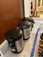 Three vacuum coffee canisters made of stainless steel with black plastic lids and bases, arranged in line on a countertop.