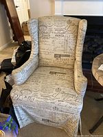 Full view of a beige wing chair with black vintage handwriting and postal text upholstery.
