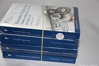 Four sealed paperback Great Courses lecture series books stacked and secured with a rubber band. Titles focus on engineering, technology, and astronomy.