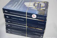 Photo showing six academic lecture series books on economics topics stacked and sealed together with a rubber band, titles visible on spines.