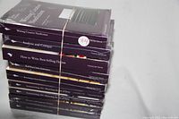 Photo showing the stacked nine books wrapped in original sealed plastic, titles visible on spines, secured with a rubber band.