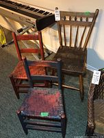 Photo showing three antique wooden chairs: two with woven wicker seats in different colors and one with a solid wood seat with wear and chips. They have spindle backrests and visible signs of age.