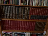 Two long shelves fully packed with Encyclopedia Britannica volumes in varied colors, showing Micropaedia, Macropaedia, Medical and Health, and general encyclopedic volumes.