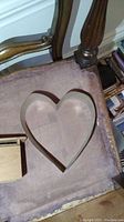 Large wooden heart frame positioned on a vintage wooden chair with padded seat.