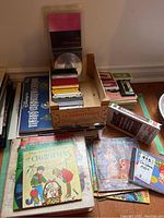 Photo showing wooden crate filled with children's cassette tapes along with stacked LP records and some CDs and VHS cases nearby.