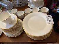 Stack of dinner and smaller plates with teacups in the background showing the gold rim design.