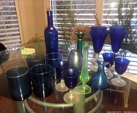 Full assortment of blue glassware on a glass table near window with natural light showing different shades and styles.