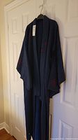 Full length photo of the navy blue kimono with red designs hanging on a hanger.