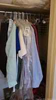 Men's dress shirts hanging in a closet, some in protective dry cleaning bags, with various colors including blue, white, and plaid.