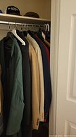 Closet view showing several men's coats and sport coats including dark and beige colored pieces hung on a rod