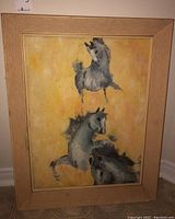 Full view of signed painting on board showing three gray horses against a yellow background within a light wood frame with visible wear.