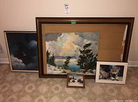 View showing all five items: two oil paintings leaning against wall, wooden plaque, framed print of bird, and empty wood frame with backing.