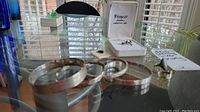 Photo showing four sterling silver round bangle bracelets with smooth and patterned textures and two rings, one in a box labeled Fiancée Jewelry.