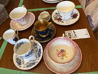 Top view showing six teacups and six saucers with various floral and gold trims arranged on a wooden surface.