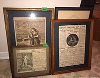 Three antique framed clippings featuring vintage advertisements and a framed print, displayed on a wooden floor, showing overall condition and framing style