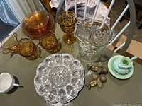 Vintage amber glass dishes, clear cut glass pitcher, deviled egg tray, two metal bird figurines, and vintage Avon green jade perfume bottle with dish visible on table.