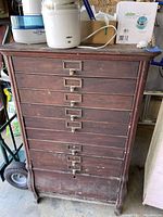 Front view showing eight-drawer wooden cabinet with metal label holders and pulls, dark finish and bracket feet