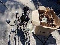 Photo showing the chandelier with six outward arms and metal sockets, frosted glass shades in a box nearby.