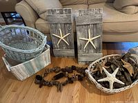 Photo showing 2 rectangular wooden wall plaques with starfish, 3 baskets, driftwood pieces, decorative starfish, and seed pod garland arranged on floor