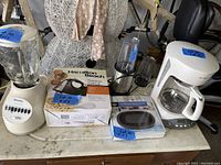 Wide view of all kitchen appliances on table including blender, mixer, scale, and coffee maker