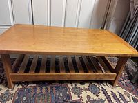 Full view of mission style rectangular wooden coffee table on a patterned rug, showing the table's solid structure and slatted lower shelf.