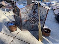 Photo of metal fireplace screen, copper pot, ash bucket and broom on pavement under daylight