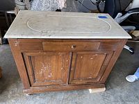 Front view of antique wooden washstand with white marble top, showing scratches, drawer, and double-door cabinet.