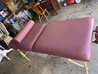 Earthlite Spirit massage table with maroon vinyl upholstery, wooden adjustable legs, and bolster pillow in garage environment.