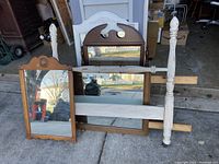 Photo of several wooden framed mirrors leaning upright and the wooden bed headboard with turned posts leaning on the right side